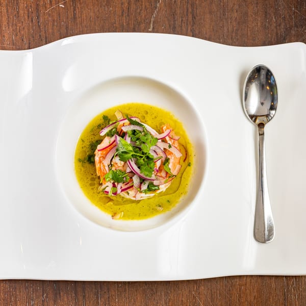 Shrimp ceviche with red onion and cilantro in a vibrant green sauce, served on a white plate.