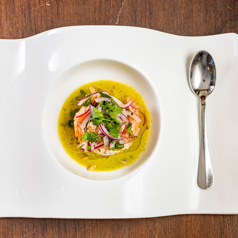 Shrimp ceviche with red onion and cilantro in a vibrant green sauce, served on a white plate.