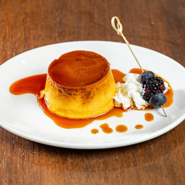 Flan dessert with caramel sauce, whipped cream, and a skewer of blueberries and blackberries.