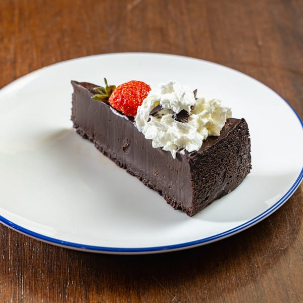 A slice of rich chocolate cake topped with whipped cream, chocolate shavings, and a fresh strawberry.