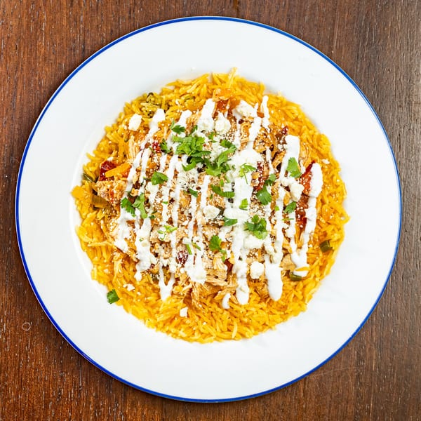 Mexican rice dish with shredded chicken, white sauce, crumbled cheese, and cilantro on a white plate.
